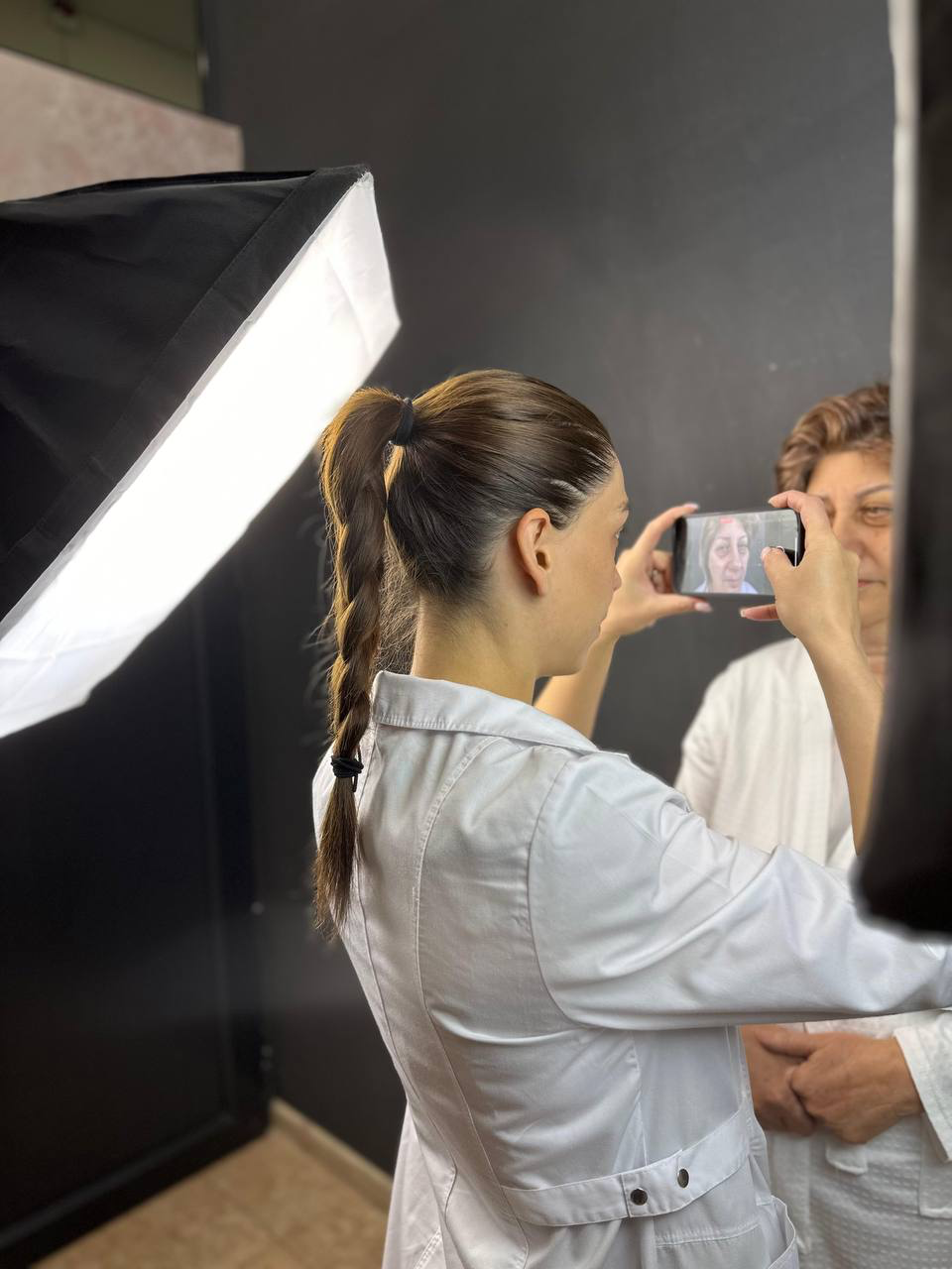 Clinic staff photographing an adult patient's face with photographic lighting and a backdrop.